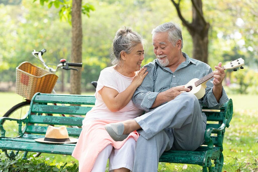 Sage Oak of Denton | Senior couple sitting on a park bench playing ukulele