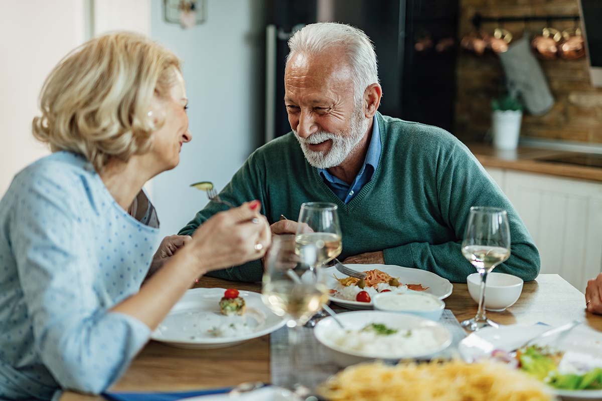 Sage Oak of Denton | Happy senior couple enjoying in conversation while eating at dining table.