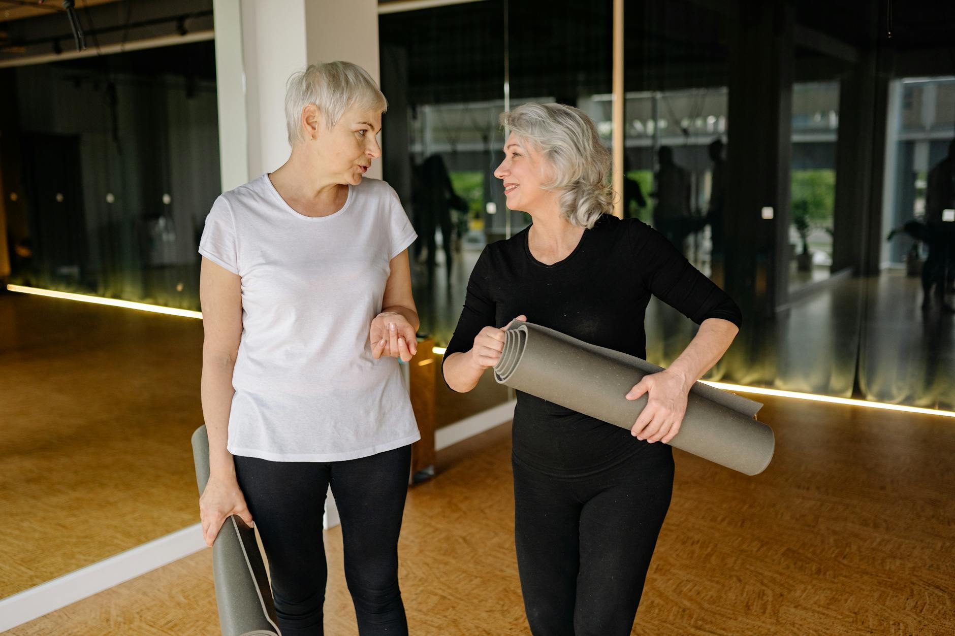 elderly women holding yoga mats while having a conversation
