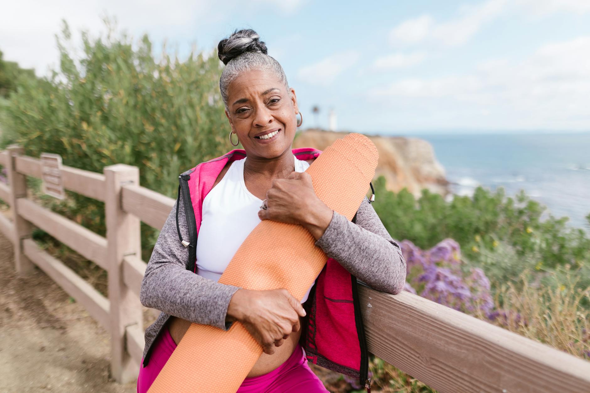 waman holding a yoga mat leaning on a wooden fence